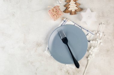 Christmas table setting. Top view of empty grey plate with black cutlery and craft wooden decorations on light table. Event table decoration. 