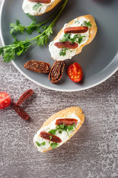 Kanepe, kızarmış ekmekli crostini, krem peynir, kurutulmuş domates, tabakta otlar. Kahvaltı için el yapımı lezzetli sandviçler..