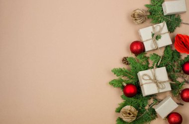 Noel süslemeleri konsepti. Üst manzara hediye kutuları el sanatları kağıdına sarılıyor, kırmızı mücevherler, çam dalları ve bej arka planda boş alan olan kurdeleler. Xmas kutlaması, kış tatili hazırlıkları.