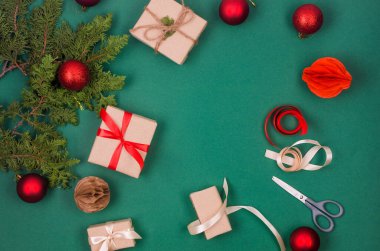Noel süslemeleri konsepti. Üst manzara hediye kutuları el sanatları kağıdına sarılı, kırmızı takılar ve yeşil arka planda kurdele. Xmas kutlaması, kış tatili hazırlıkları. 