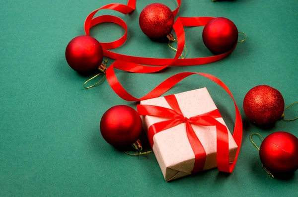 Christmas decorations concept. Top view gift boxes wrapping in craft paper, red baubles and ribbon on green background. Xmas celebration, preparation for winter holidays.