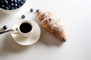 Freshly baked French croissant for breakfast on plate and cup of hot coffee on white table. Tasty croissants.