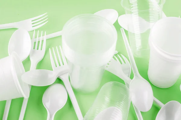 White Disposable cups, plates, forks, knives on light green background close-up - Environmental problem concept