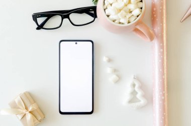 Beyaz ekranlı telefon, şekerli fincan kakao ve masada Noel süslemesi. Hedef belirleme, bilgilendirme kavramı. Sıcak bir tatil ve yeni yıl konsepti.