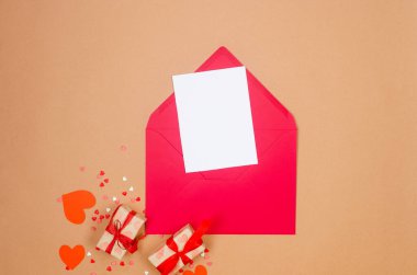 Kırmızı zarfta boş beyaz kağıt, bej arka planda hediye kutuları ve kalpler. Sevgililer Günü konsepti, düğünler, nişanlar, Anneler Günü, doğum günü. Metin için yeri olan tebrik kartı 