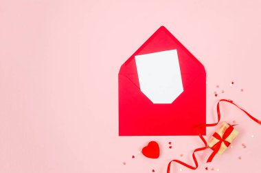 Kırmızı zarfta boş beyaz kağıt, pembe arka planda hediye kutuları ve kalpler. Sevgililer Günü konsepti, düğünler, nişanlar, Anneler Günü, doğum günü. Metin için yeri olan tebrik kartı 