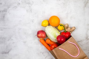 Top view of grocery bag with organic fresh vegetables and fruits on light grey background. Shopping or delivering healthy food. Sustainable lifestyle, good, real plant-based foods. Veganuary concept