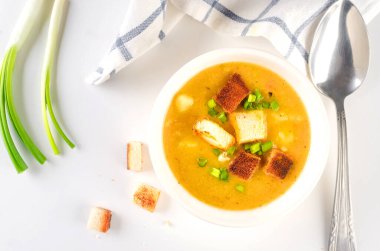 Split pea soup with croutons and green onion in a bowl on white table. Healthy homemade thick soup in white bowl for winter lunch.