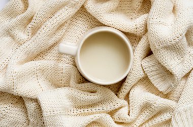 White cup of coffee with milk on a warm white knitted blanket. Winter concept.