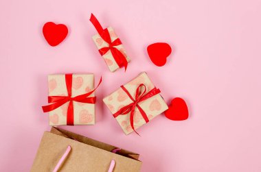 Kırmızı kalpler ve hediye kutuları el işi kağıdına ve pembe arka plana kırmızı kurdele bağlamış. Sevgililer Günü konsepti, düğünler, nişanlar, Anneler Günü, doğum günü. Metin için yeri olan tebrik kartı 