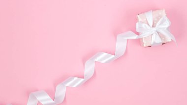Gift box in wrapping paper tied long white ribbon on pink background. Concept of the St. Valentine's day, weddings, engagements, Mother's Day, birthday. Greeting card with place for text 