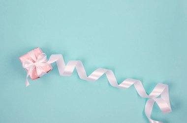 Gift box in wrapping paper tied long white ribbon on blue background. Concept of the St. Valentine's day, weddings, engagements, Mother's Day, birthday. Greeting card with place for text 