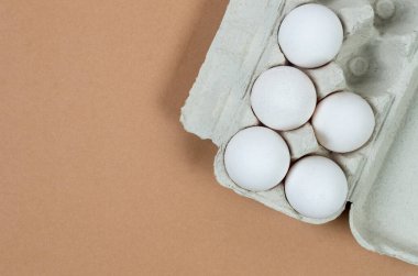 Fresh white chicken eggs in a cardboard tray close-up on beige background. Group of five eggs.