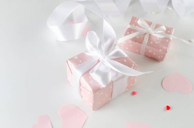 Many pink gifts boxes with white ribbon and paper pink hearts on white background. Concept of Valentine day. Greeting card for Valentine,  Mother day or birthday.