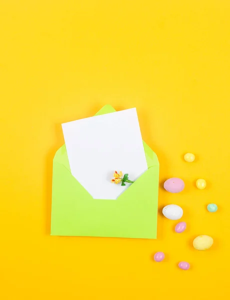 イースターカラフルなキャンディーチョコレートの卵と黄色の背景に空白のカードを持つ薄い緑の封筒 イースター休暇と伝統的な概念 休日の準備 — ストック写真