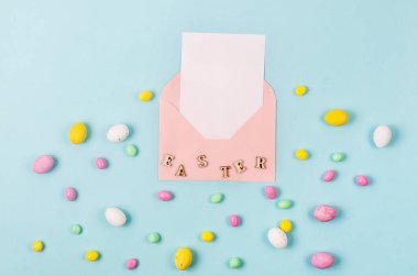 Mavi arka planda renkli paskalya yumurtaları ve içinde mesaj yeri olan boş bir kart olan pembe zarf. Paskalya tatili ve gelenek kavramı. 