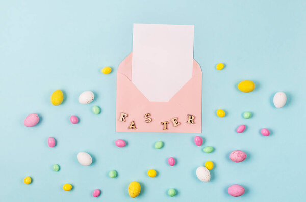 Colorful candy easter eggs on blue background and pink envelope with blank card with place for text. Easter holiday and tradition concept. 