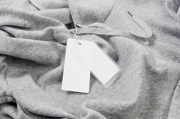 空空的白色纸板标签与字符串在灰色球衣帽衫 在衣服上贴上空白的模型 以放置你的设计 价格标签 地址标签 购物概念 — 图库照片