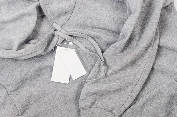 Empty white cardboard tag with string ongrey jersey hoodie. label blank mockup on a clothes, to place your design.  Price tag, sale, address label. Shopping concept.