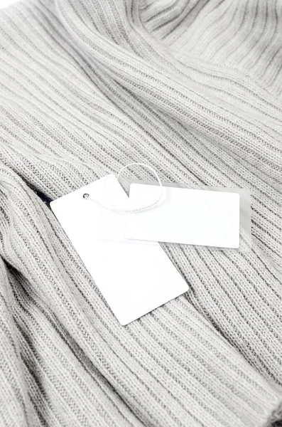 Empty white cardboard tag with string on grey sweater. Label blank mockup on a clothes, to place your design.  Price tag, sale, address label. Shopping concept.