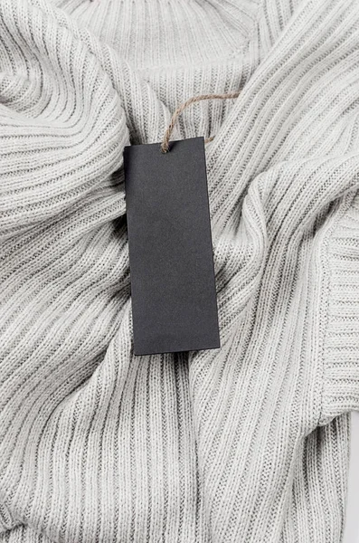 Empty black cardboard tag with string on grey sweater. Label blank mockup on a clothes, to place your design.  Price tag, sale, address label. Shopping concept.