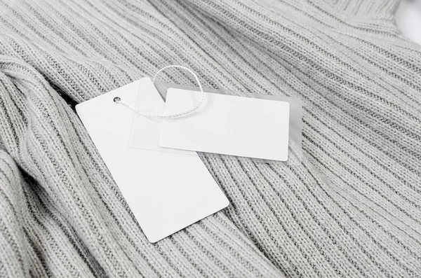 Empty white cardboard tag with string on grey sweater. Label blank mockup on a clothes, to place your design.  Price tag, sale, address label. Shopping concept.