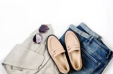 Mavi kot, büyük beden kazak, bej süet mokasen ya da beyaz arka planda yatan düz ayakkabılar. Kadınların günlük kıyafetlerinin genel görünüşü. Moda kadın kıyafetleri. 