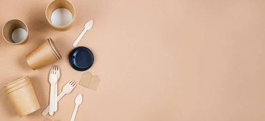 Tek kullanımlık kağıt bardaklar, tahta çatallar ve bej arka planda kaşıklar. Kraft kağıt gıda ambalajı ve ahşap çatal bıçak takımı. Doğal malzemeden sokak yiyecekleri ambalajı. 