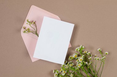 İçinde mesaj ve bej arka planda papatya demeti için boş beyaz kart olan pembe bir zarf. Boş davet veya kopyalama alanı olan tebrik kartı modeliName