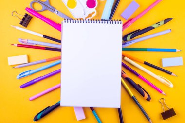Okul defteri ve sarı arka planda çeşitli kırtasiye malzemeleri. Okulda okumak için malzemeler. Flatlay, maket yap. Renkli kırtasiye iskeleti. Okul konseptine dönelim.. 