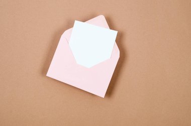 Üzerinde bej arka planda mesaj için boş beyaz kart olan pembe bir zarf. Boş davet veya kopyalama alanı olan tebrik kartı modeliName