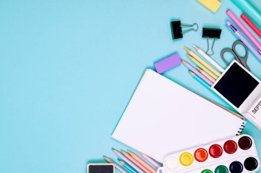 Okul defteri ve mavi arka planda çeşitli kırtasiye malzemeleri. Okulda okumak için malzemeler. Flatlay, maket yap. Renkli kırtasiye iskeleti. Okul konseptine dönelim.. 
