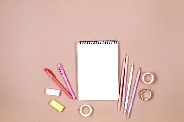School notebook and various stationery for girls in pink colors on beige background. Supplies for studying at school. Flatlay,  mock up. Frame of colorful stationery. Back to school concept.