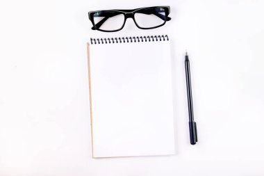 Boş defter, beyaz arka planda kalem ve gözlük. Okulda ya da işte okumak için malzemeler. 