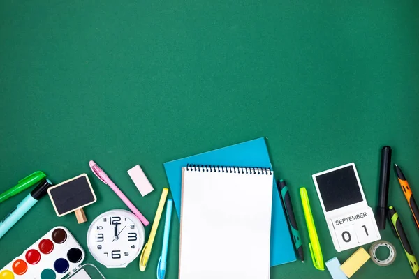 School notebook and various stationery on green background. Supplies for studying at school. Flatlay,  mock up. Frame of colorful stationery. Back to school concept.