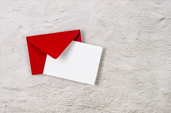 Red envelope with empty white card for text on grey concrete background. Blank invitation or greeting card mockup with copy space