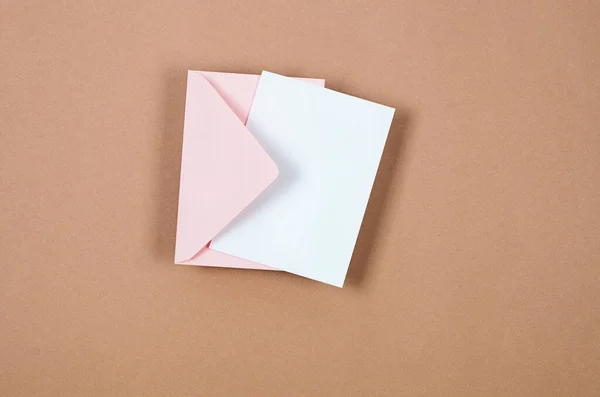Pink envelope with empty white card for text on beige background. Blank invitation or greeting card mockup with copy space