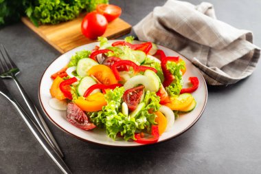 Taze domatesli sebze salatası, salatalık, soğan, beyaz tabakta marul. Karanlık taş arka plan. Lezzetli ve sağlıklı yemek kavramı.. 