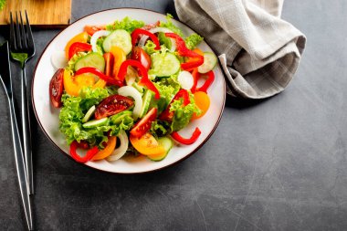 Taze domatesli sebze salatası, salatalık, soğan, beyaz tabakta marul. Karanlık taş arka plan. Lezzetli ve sağlıklı yemek kavramı.. 