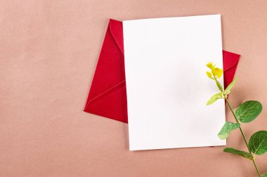 Yazı için boş beyaz kart ve bej arka planda okaliptüs dalları olan kırmızı bir zarf. Boş davet veya kopyalama alanı olan tebrik kartı modeliName