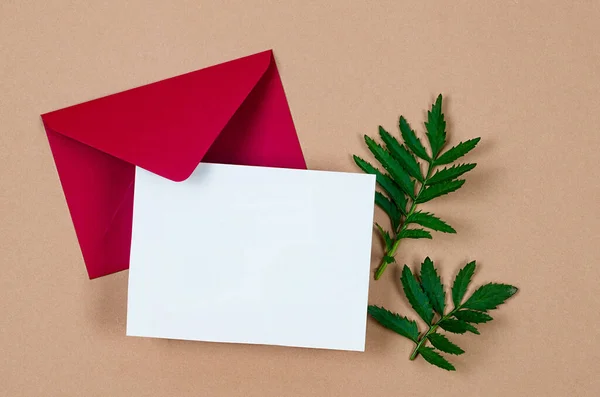 Red envelope with empty white card for text on grey concrete background. Blank invitation or greeting card mockup with copy space