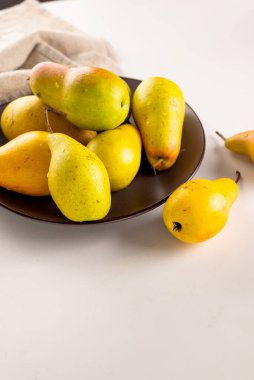 Beyaz bir masada, tabakta olgun sarı-yeşil armut. Taze armut kapağı.. 