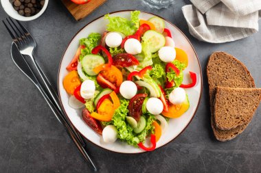 Kırmızı ve sarı domatesli salata, biber, salatalık, marul ve mozzarella. Karanlık taş arka plan. Öğle yemeği için lezzetli salata. Sağlıklı yemek.. 