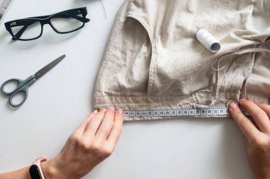 Kadın terzi keten gri pantolon dikiyor. Dikiş ve ev işi. Dairesel moda, hızlı moda, sürdürülebilir, sıfır israf yaşam tarzı konsepti