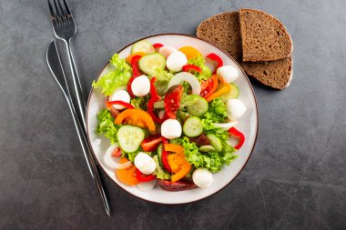 Kırmızı ve sarı domatesli salata, biber, salatalık, marul ve mozzarella. Karanlık taş arka plan. Öğle yemeği için lezzetli salata. Sağlıklı yemek.. 