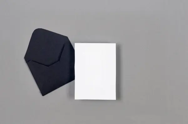 Black envelope with empty white card for text on grey background. Blank invitation or greeting card mockup with copy space