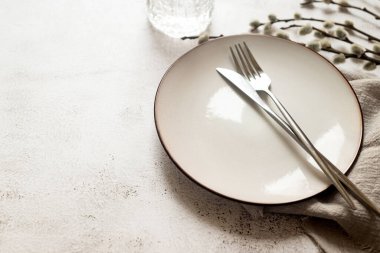 Paskalya sofrası, boş beyaz seramik tabak, çatal bıçak takımı ve beyaz masada söğüt dalları. Tarafsız renkler. Paskalya arkaplanı.