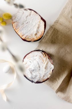 Paskalya yemeği için beyaz masaya yerleştirilmiş paskalya pastası, renkli süslemeli çikolata yumurtaları, söğüt ağacı ve tatil süslemeleri. Bahar tatili konsepti. Mutlu Paskalyalar