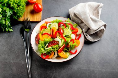 Taze domatesli sebze salatası, salatalık, soğan, beyaz tabakta marul. Karanlık taş arka plan. Lezzetli ve sağlıklı yemek kavramı.. 