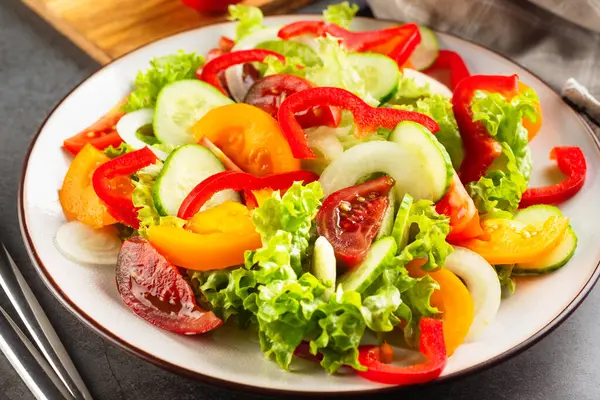 蔬菜沙拉 新鲜西红柿 白盘上的生菜 黑暗的石头背景 美味佳肴的概念 免版税图库照片
